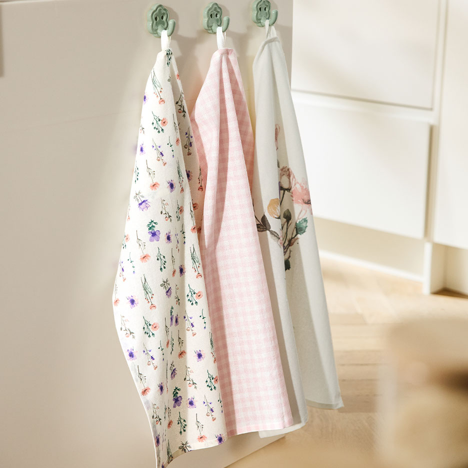 Three patterned kitchen towels hang on hooks against a light wall.