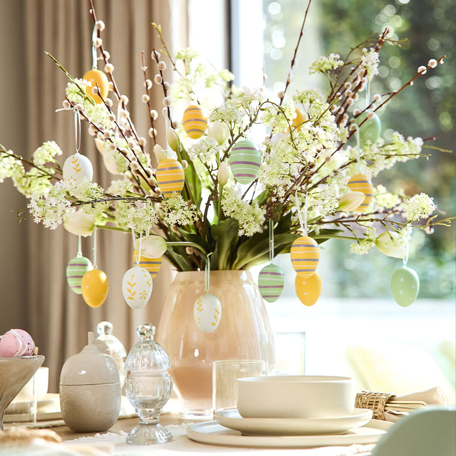 Easter table decoration with flowering branches and hanging colorful eggs.