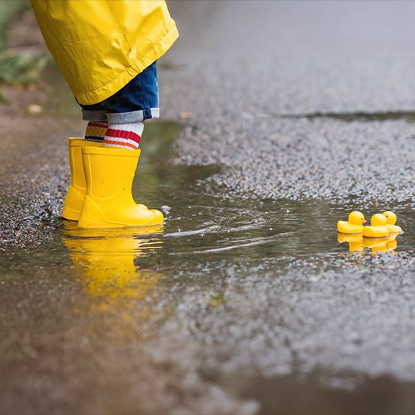 Child in yellow rain boots and jacket in a puddle with rubber ducks.