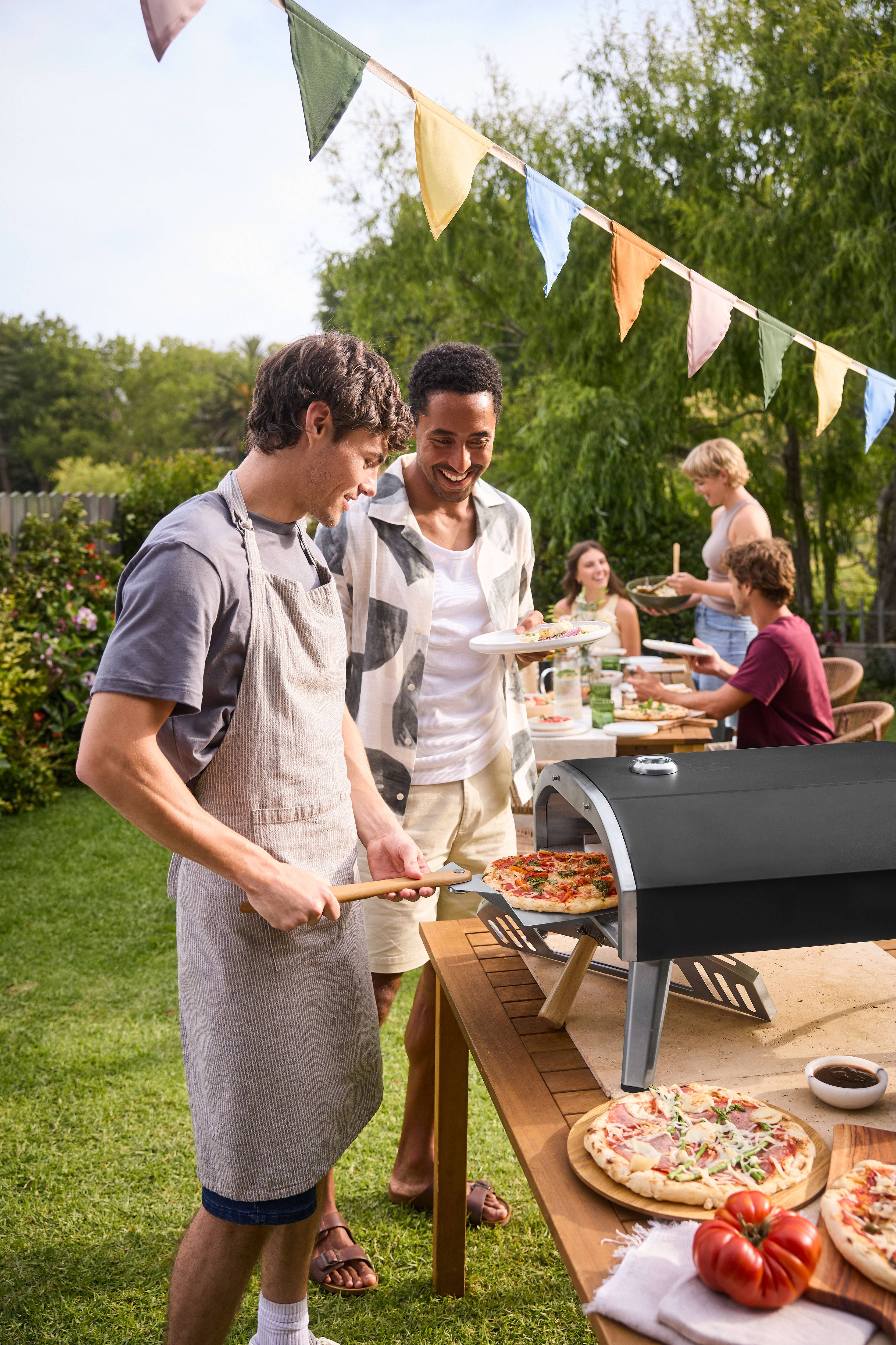 Men cooking pizza in a pizza oven at a garden party.