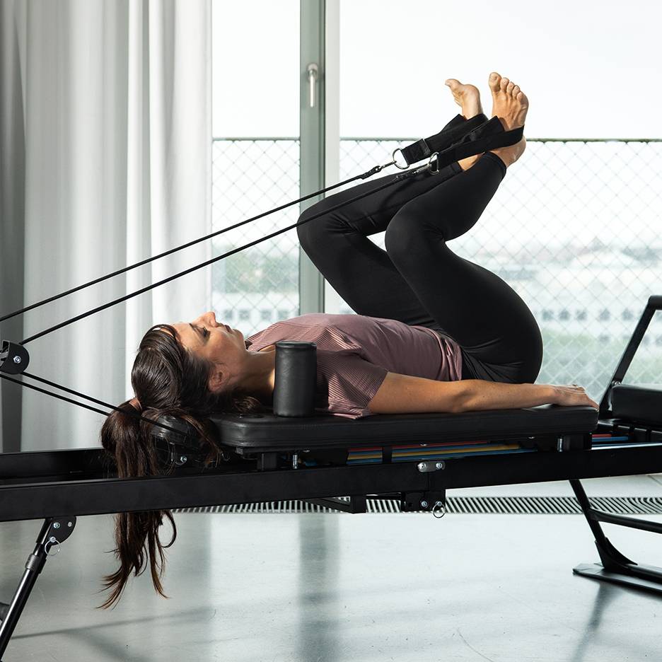 Woman exercising legs on a Pilates reformer with resistance bands.