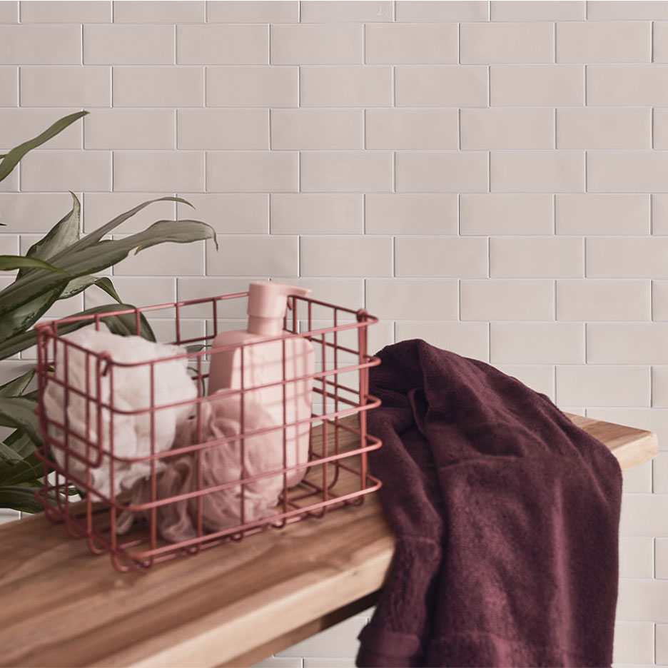 Bathroom decor with white tiles, a wooden bench, a basket with soap and towels.