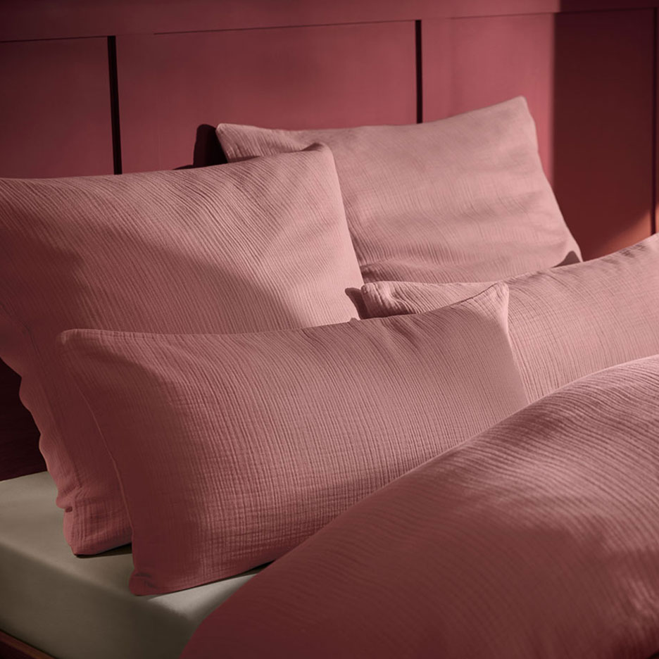 Pink muslin pillow and bedding on a bed with a wooden headboard.
