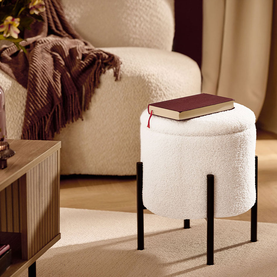 White fluffy stool with black legs, a red book, armchair, and brown blanket.