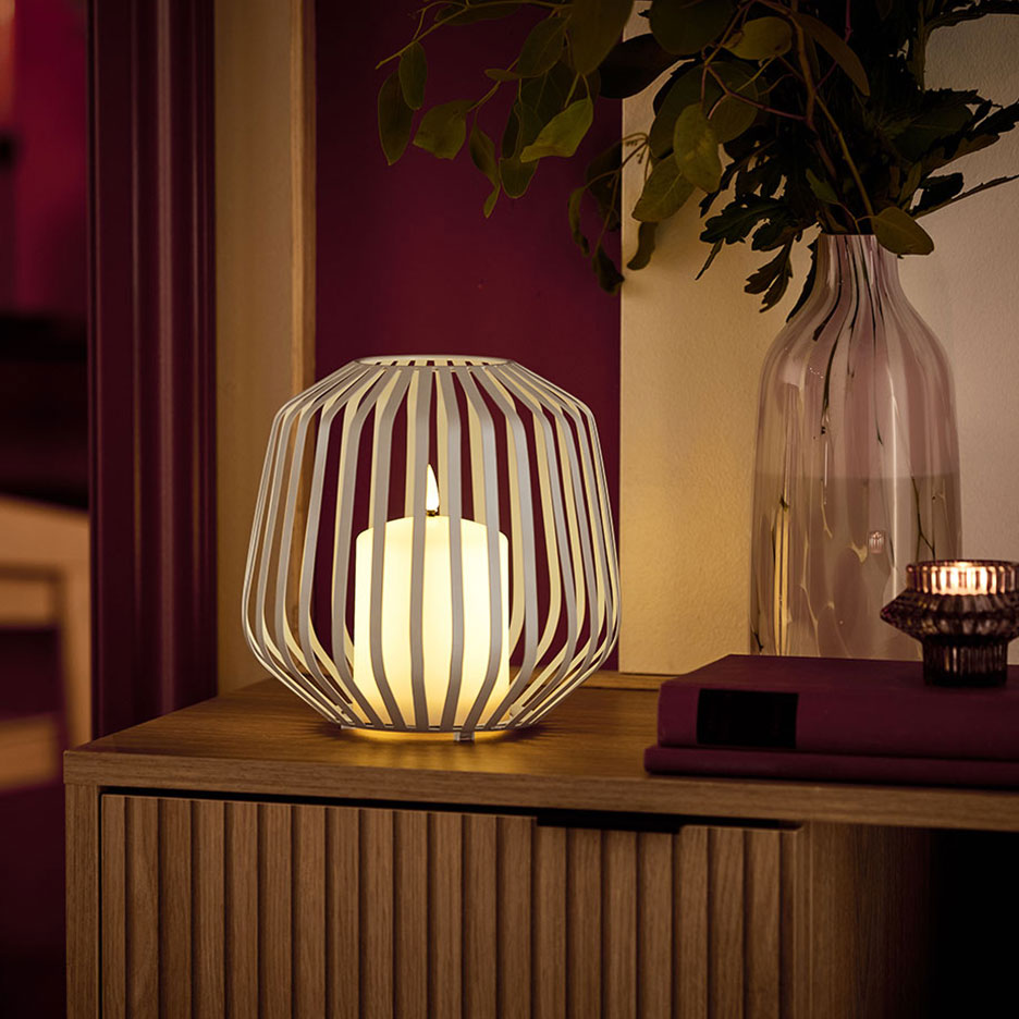 A LED candle in a white metal holder on a wooden dresser.