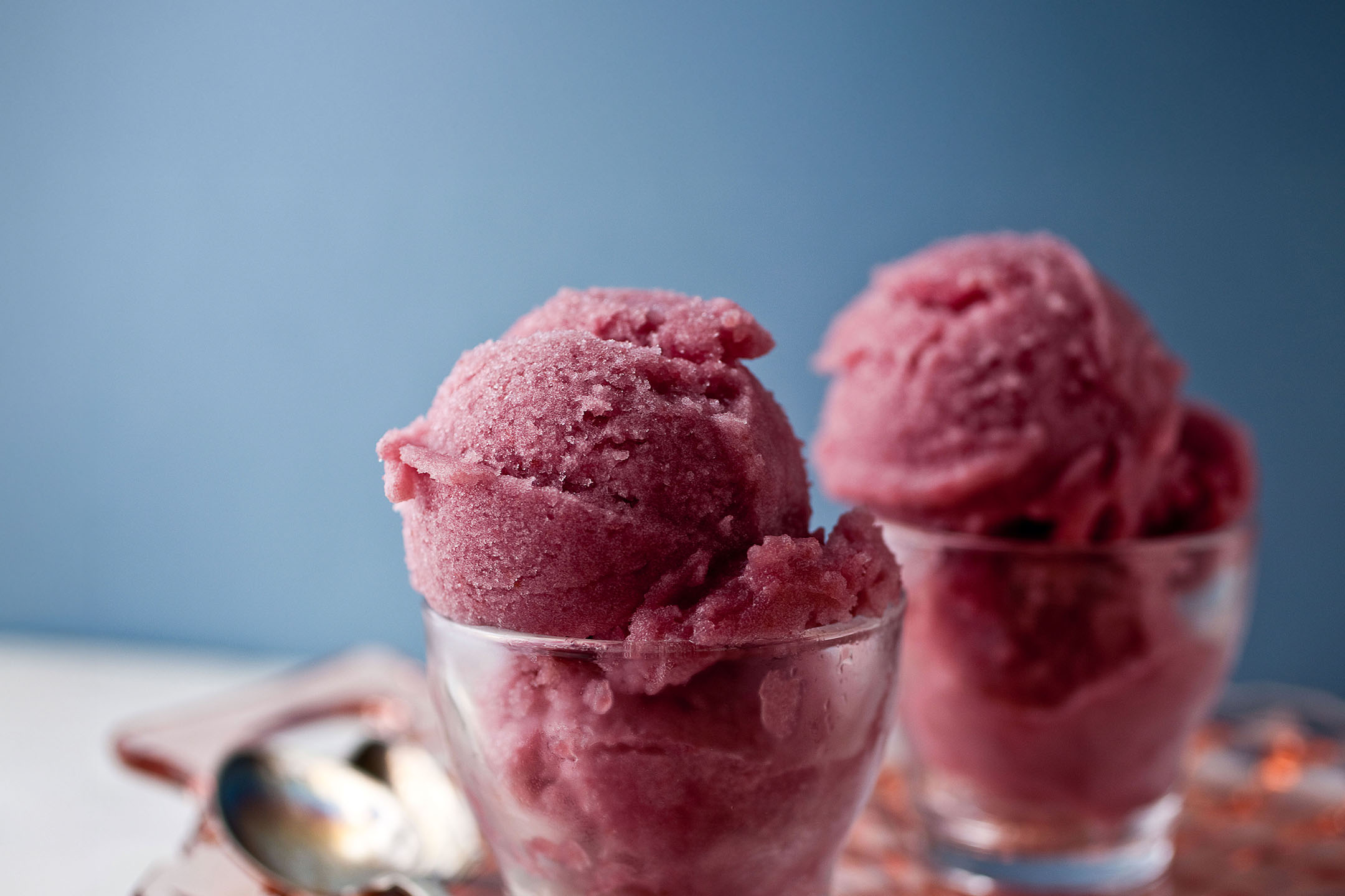 Two glasses of pink sorbet or ice cream on a white table with a blue background.