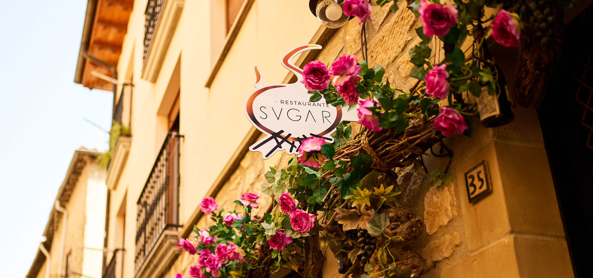 Restaurant 'SVGAR' sign with pink flowers on a stone wall