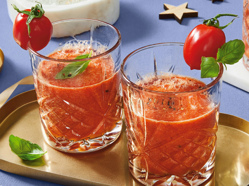 Two glasses of gazpacho with basil and cherry tomatoes.