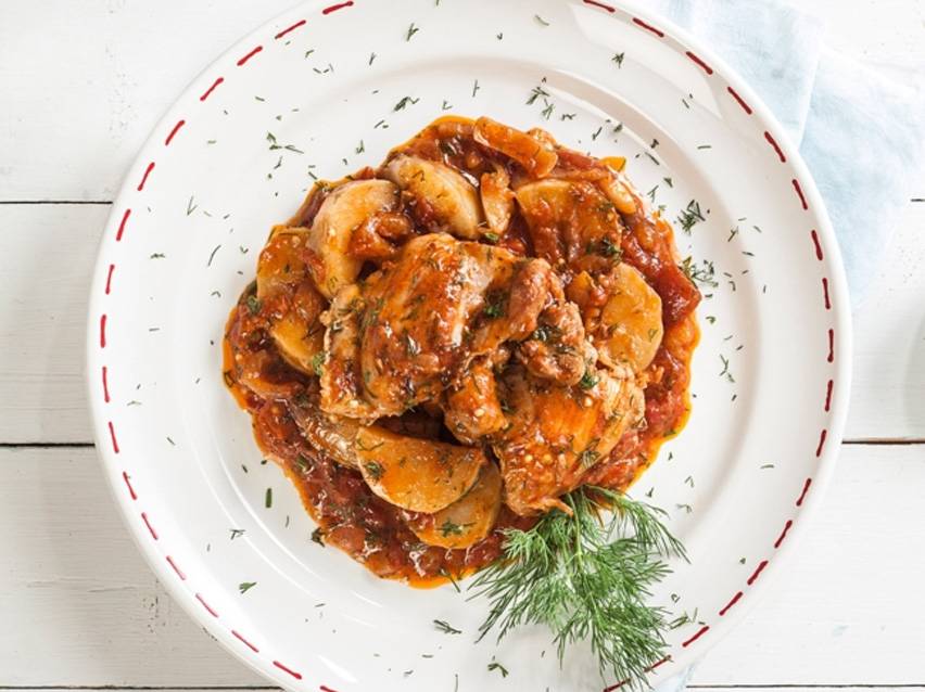 Κοτόπουλο και πατάτες σε πλούσια σάλτσα ντομάτας, γαρνιρισμένα με φρέσκο άνηθο σε λευκό πιάτο.