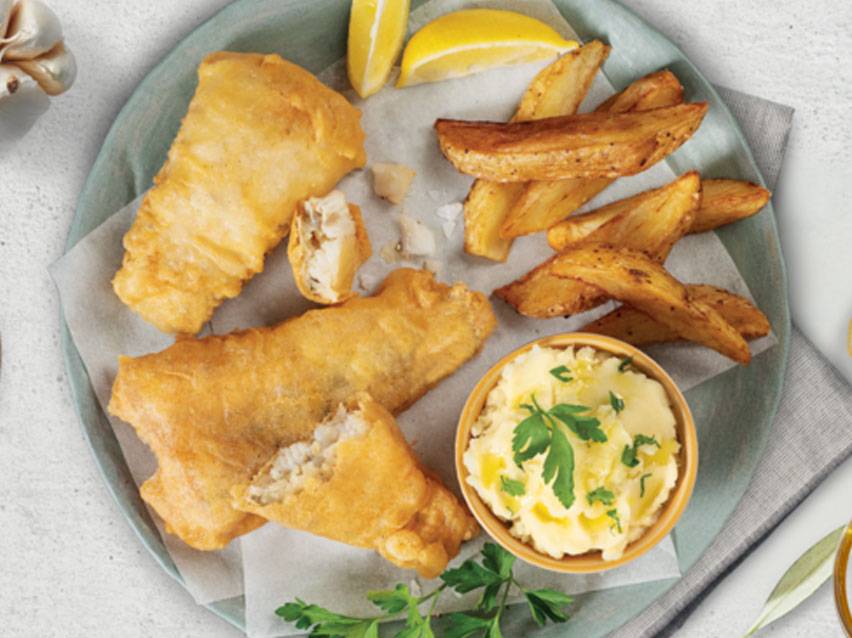Fish and chips with mashed potatoes and lemon wedges on a plate.