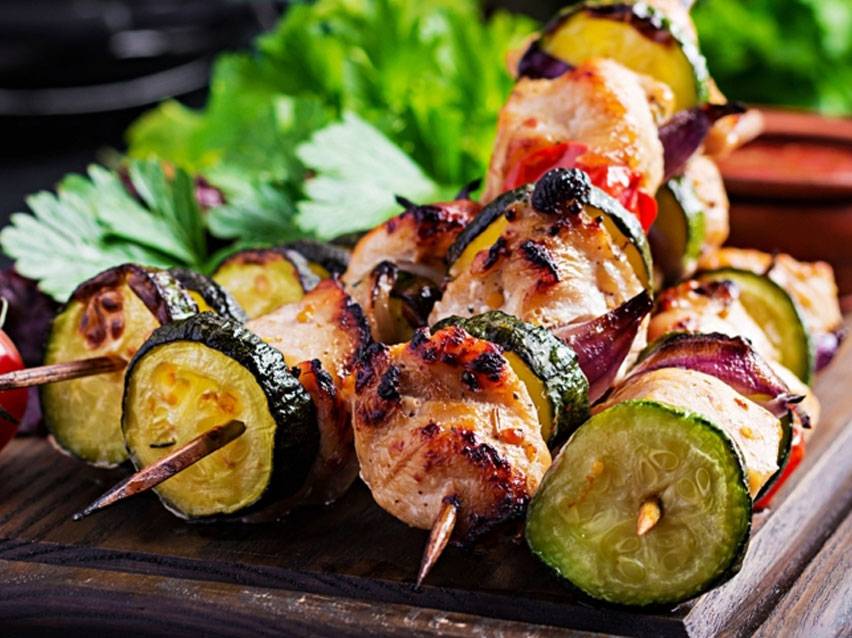 Grilled chicken and zucchini skewers on a wooden board with herbs.