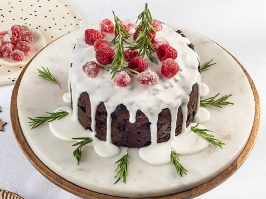 Christmas cake with icing, raspberries, and rosemary.