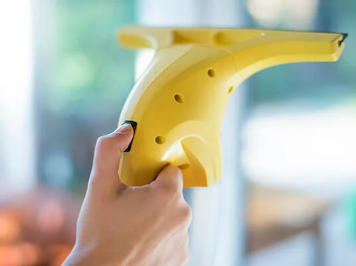 Χέρι κρατάει ένα κίτρινο ηλεκτρικό καθαριστικό παραθύρων, καθαρίζοντας ένα παράθυρο.