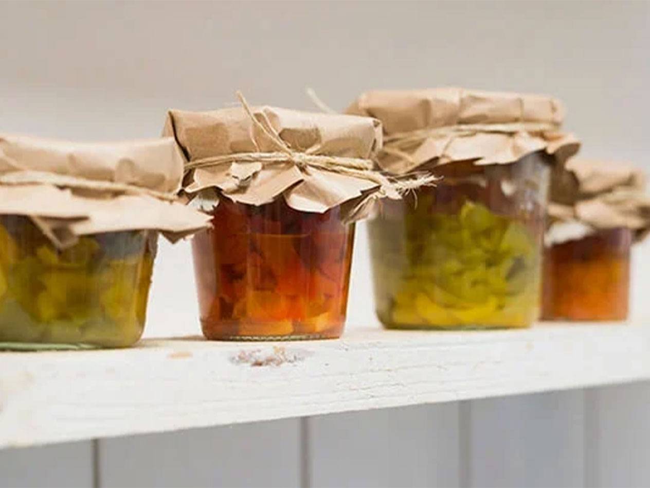 Four jars of homemade preserves, covered with brown paper and twine.