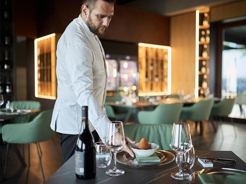 Chef serving an arancino on a plate in a restaurant.