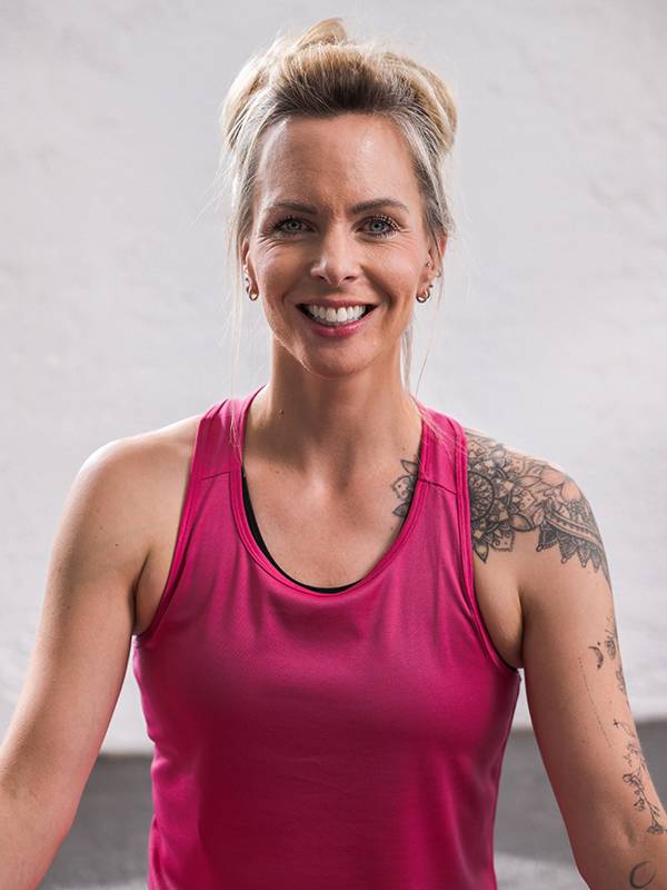 A smiling woman in a pink athletic tank top with shoulder tattoos.