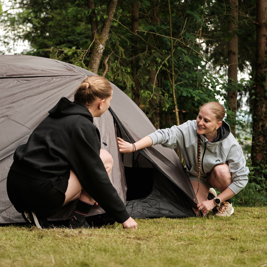 Two women setting up a tent in the woods.