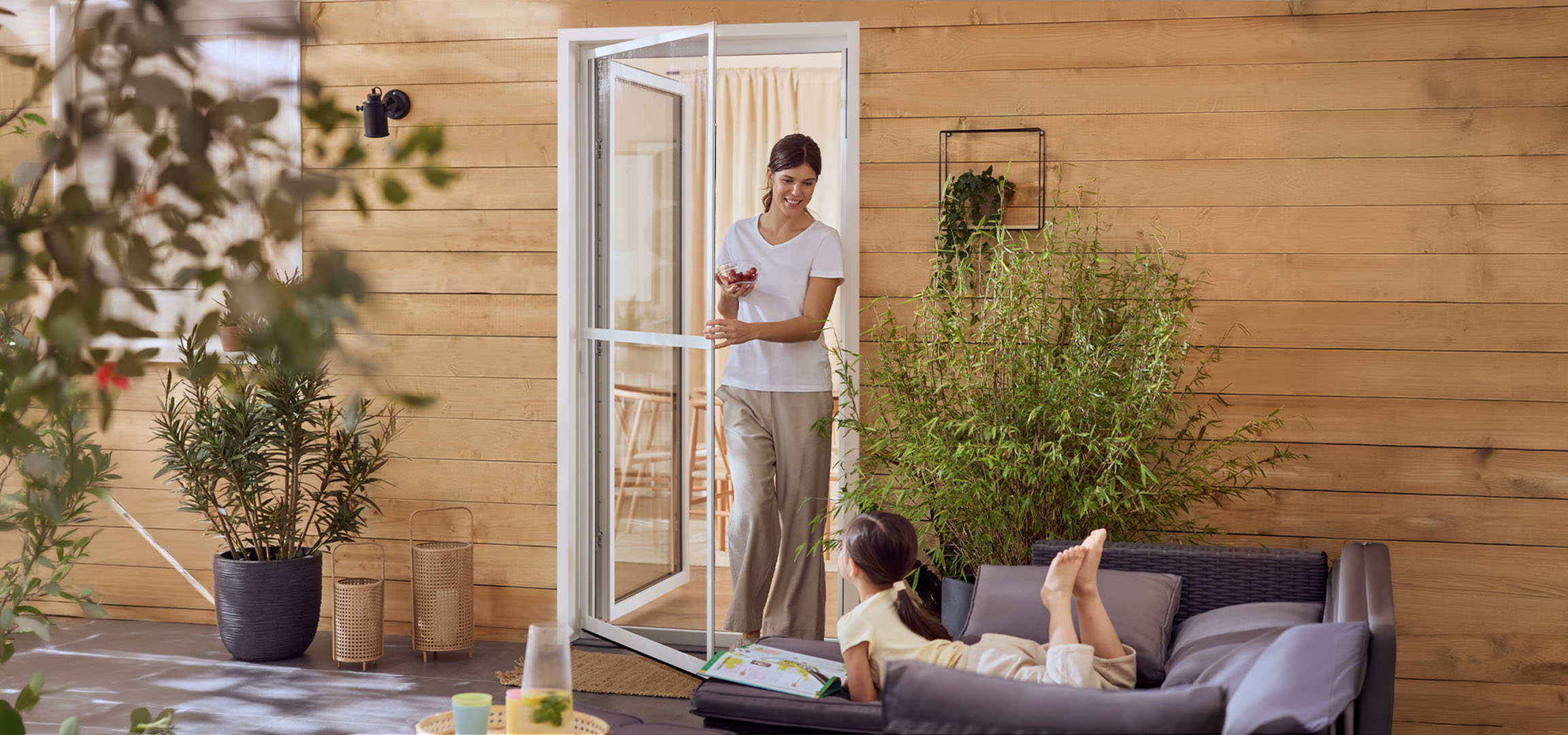 Γυναίκα και κορίτσι απολαμβάνουν μια βεράντα με έπιπλα εξωτερικού χώρου και φυτά.