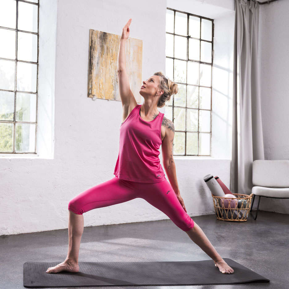 Woman doing yoga wearing pink athletic wear in a bright room.