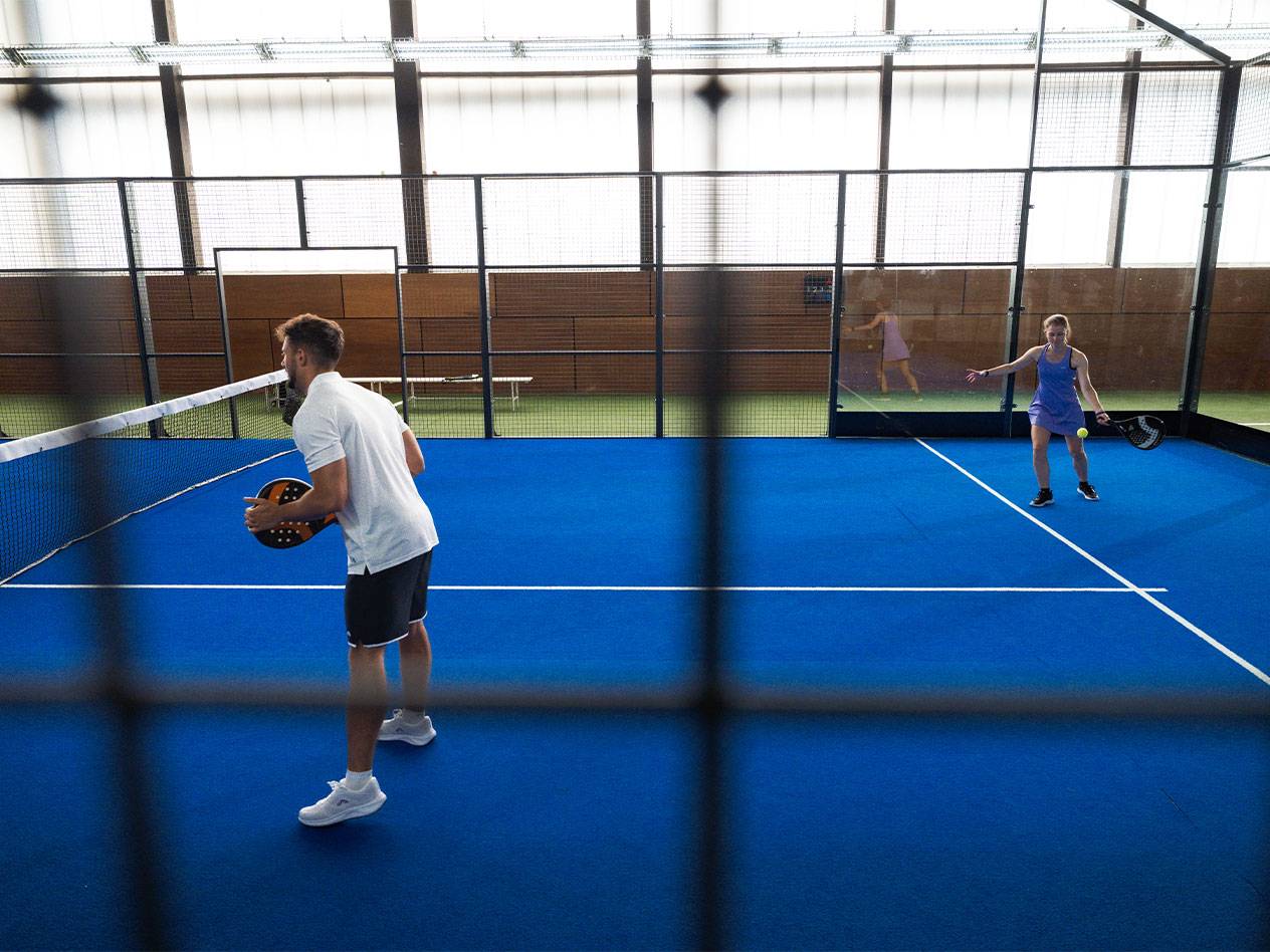 Man and woman playing padel on a blue court with rackets and a ball.