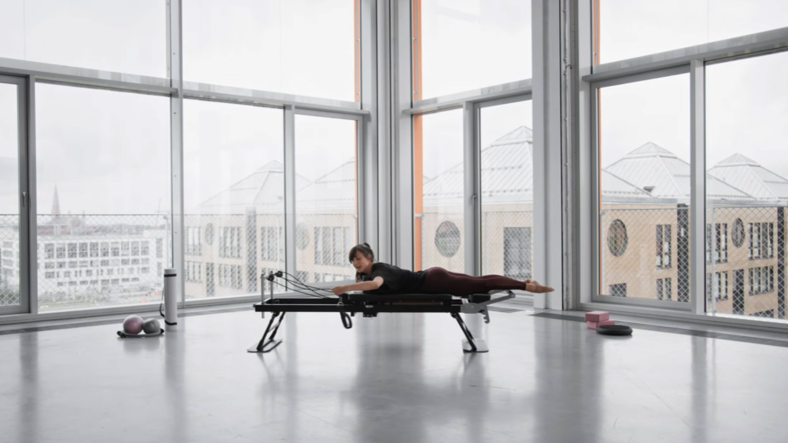 Woman doing Pilates on a reformer, with a city view.