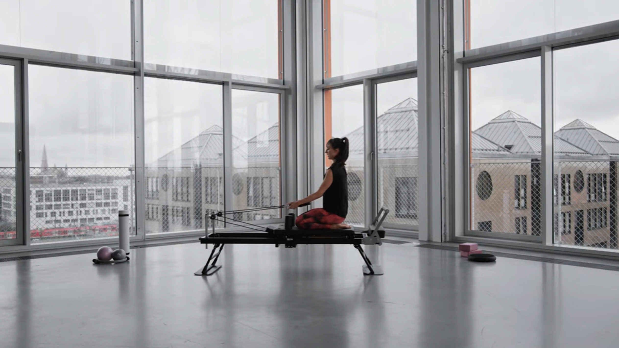 Woman doing Pilates on a reformer, with a city view.