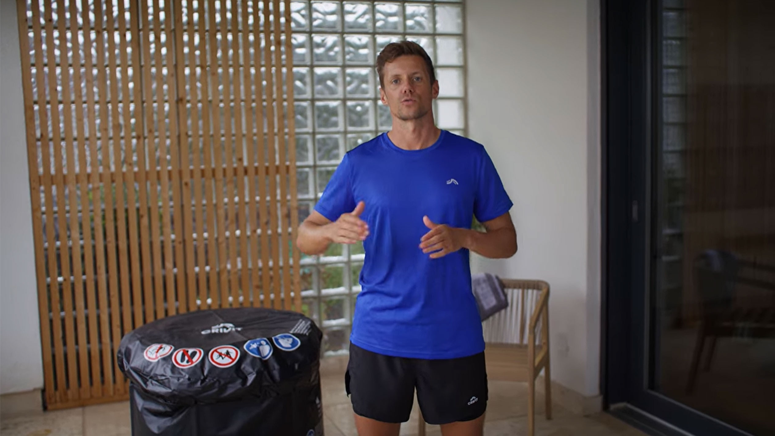 Man in blue T-shirt and black shorts, next to a black hot tub cover.