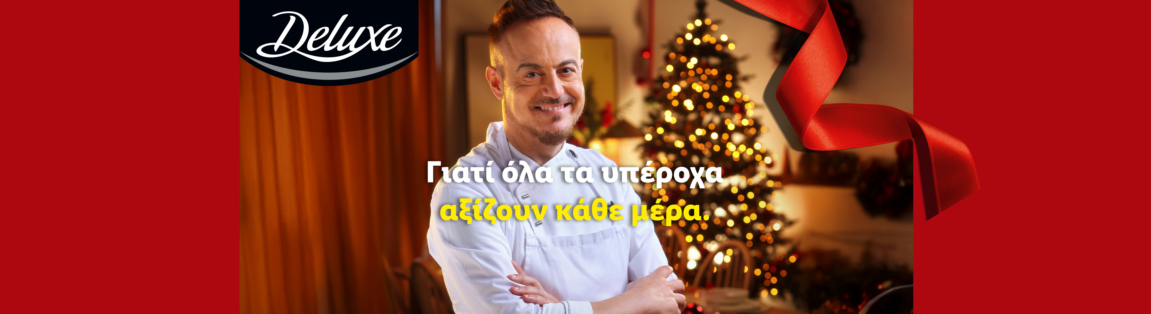 Ένας χαμογελαστός σεφ σε ένα εορταστικό σκηνικό με χριστουγεννιάτικο δέντρο και κόκκινη κορδέλα, με το κείμενο 'Deluxe' και 'Γιατί όλα τα υπέροχα αξίζουν κάθε μέρα.'