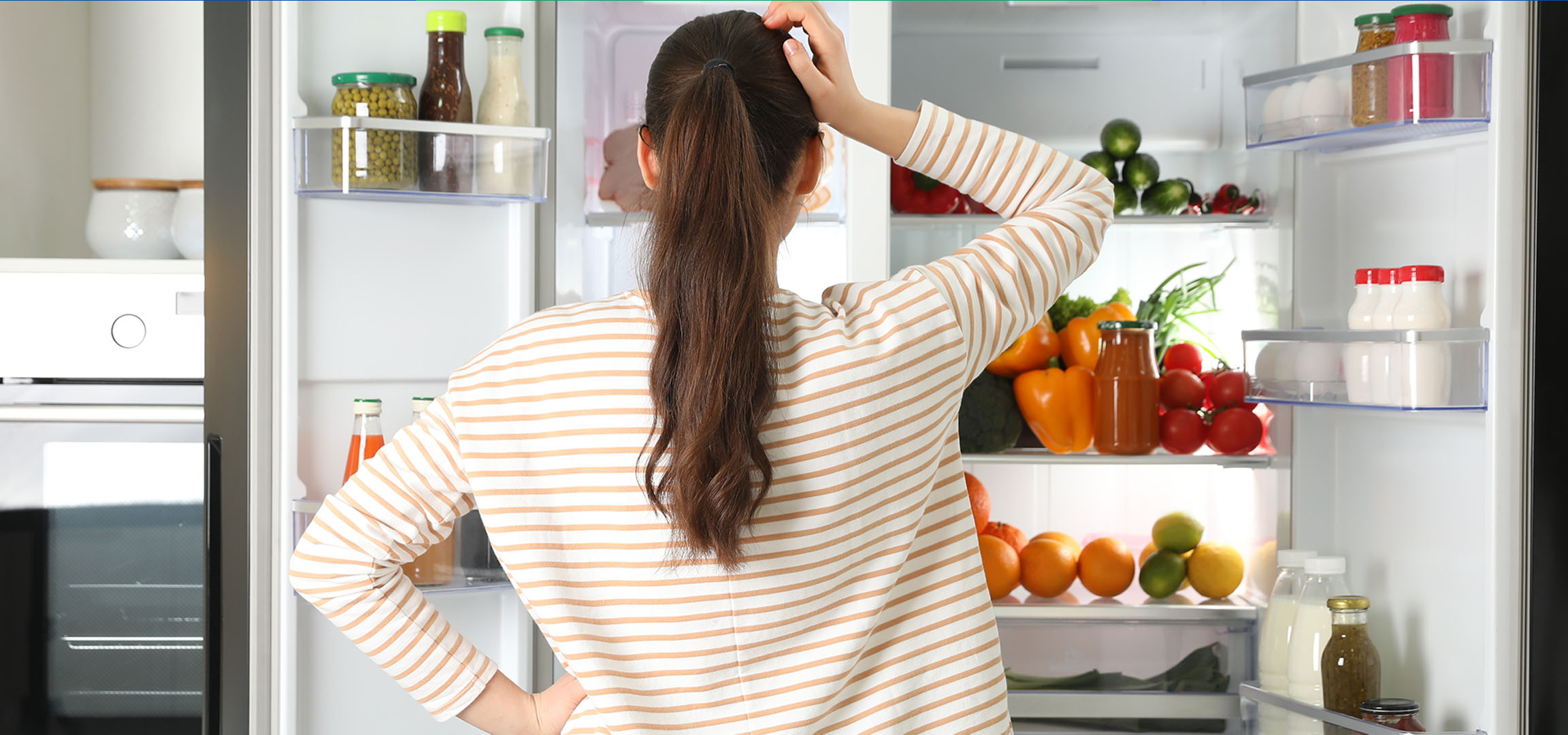Woman looking into an open fridge full of fresh vegetables, fruits, and drinks.