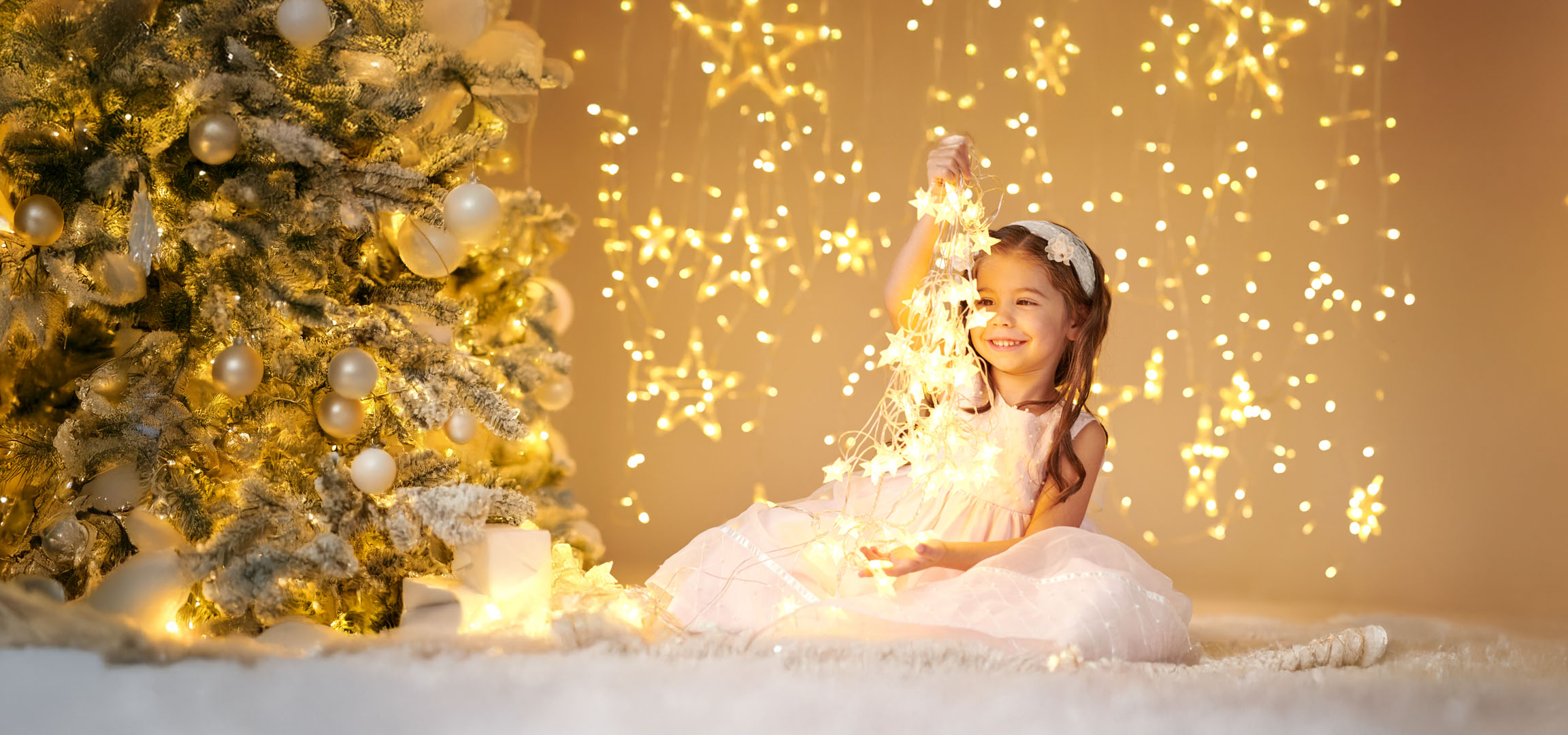 Girl with Christmas lights in front of a decorated Christmas tree.