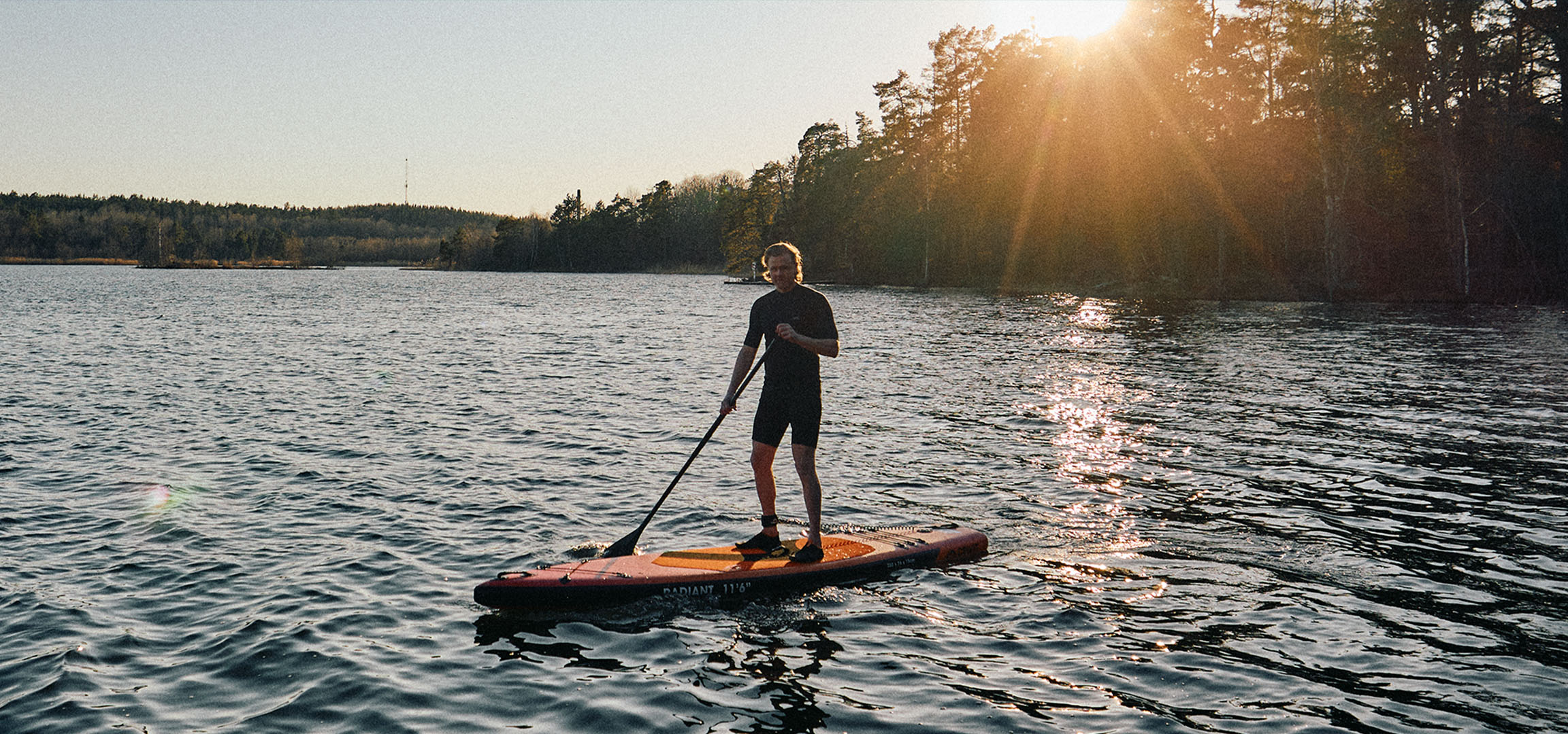 Άνδρας σε σανίδα stand up paddle σε λίμνη το ηλιοβασίλεμα.