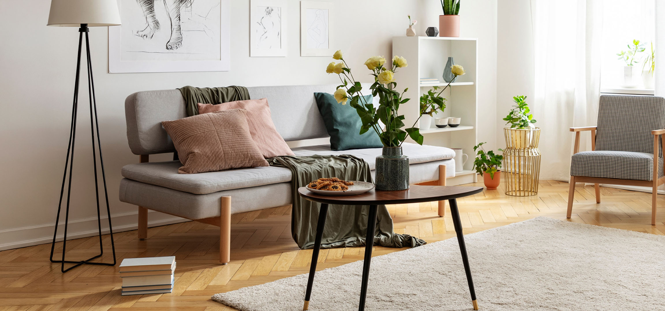 Cozy living room with a grey sofa, cushions, a coffee table with cookies, and a vase of flowers.