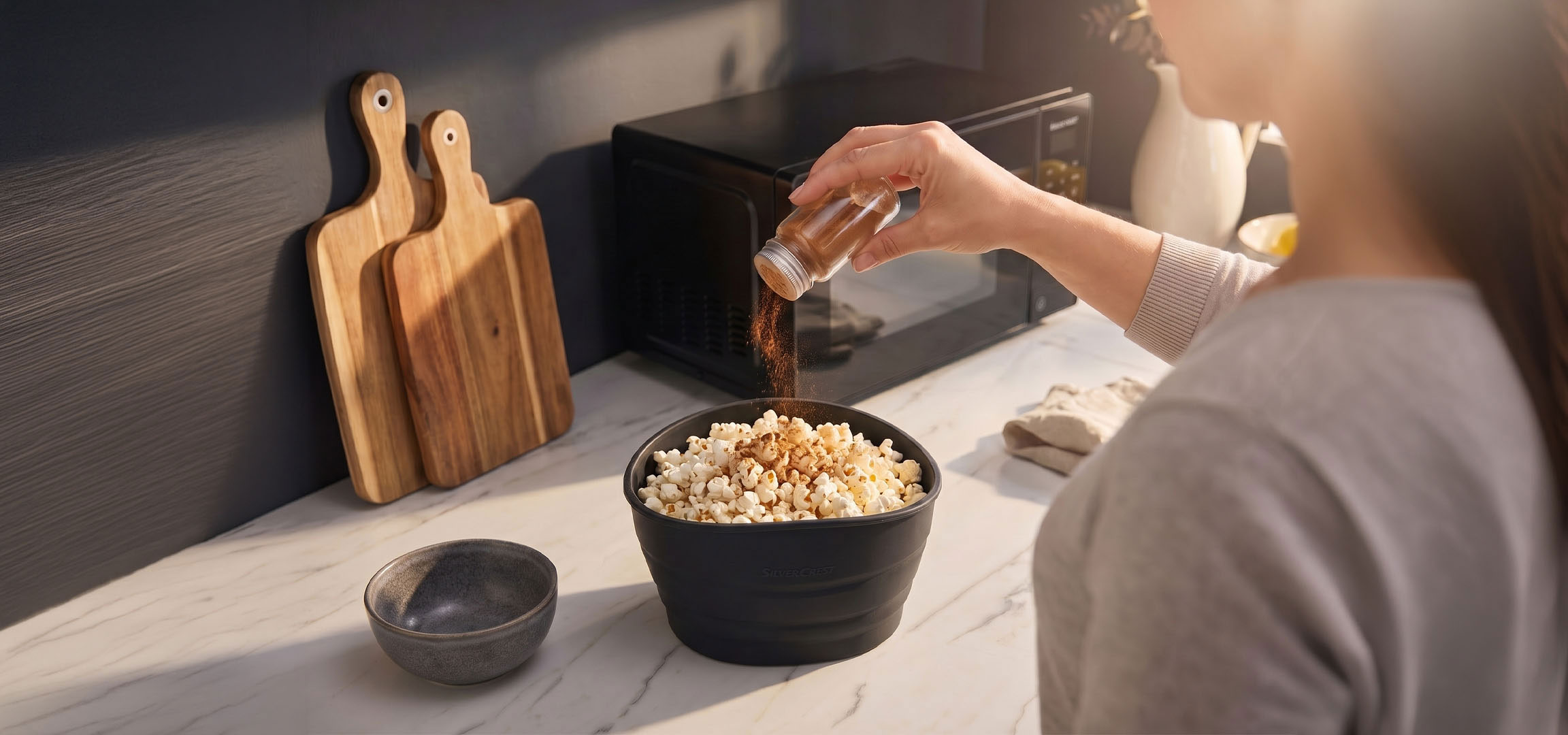 AI generated image: Popcorn in a black bowl being seasoned with spices, next to wooden cutting boards.
