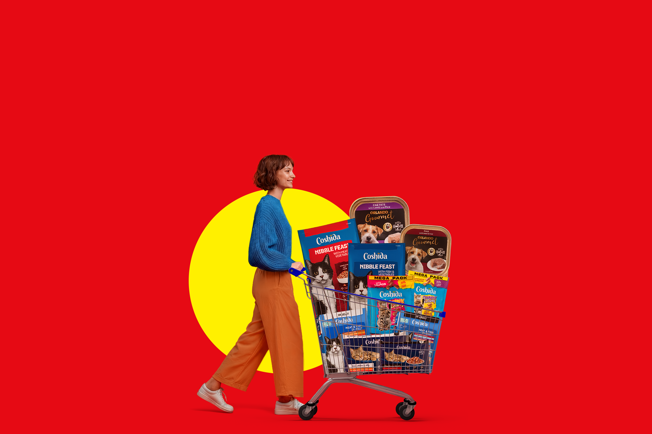 Woman pushing a shopping cart full of pet food, including pate, nibble feast, and crunchy varieties.