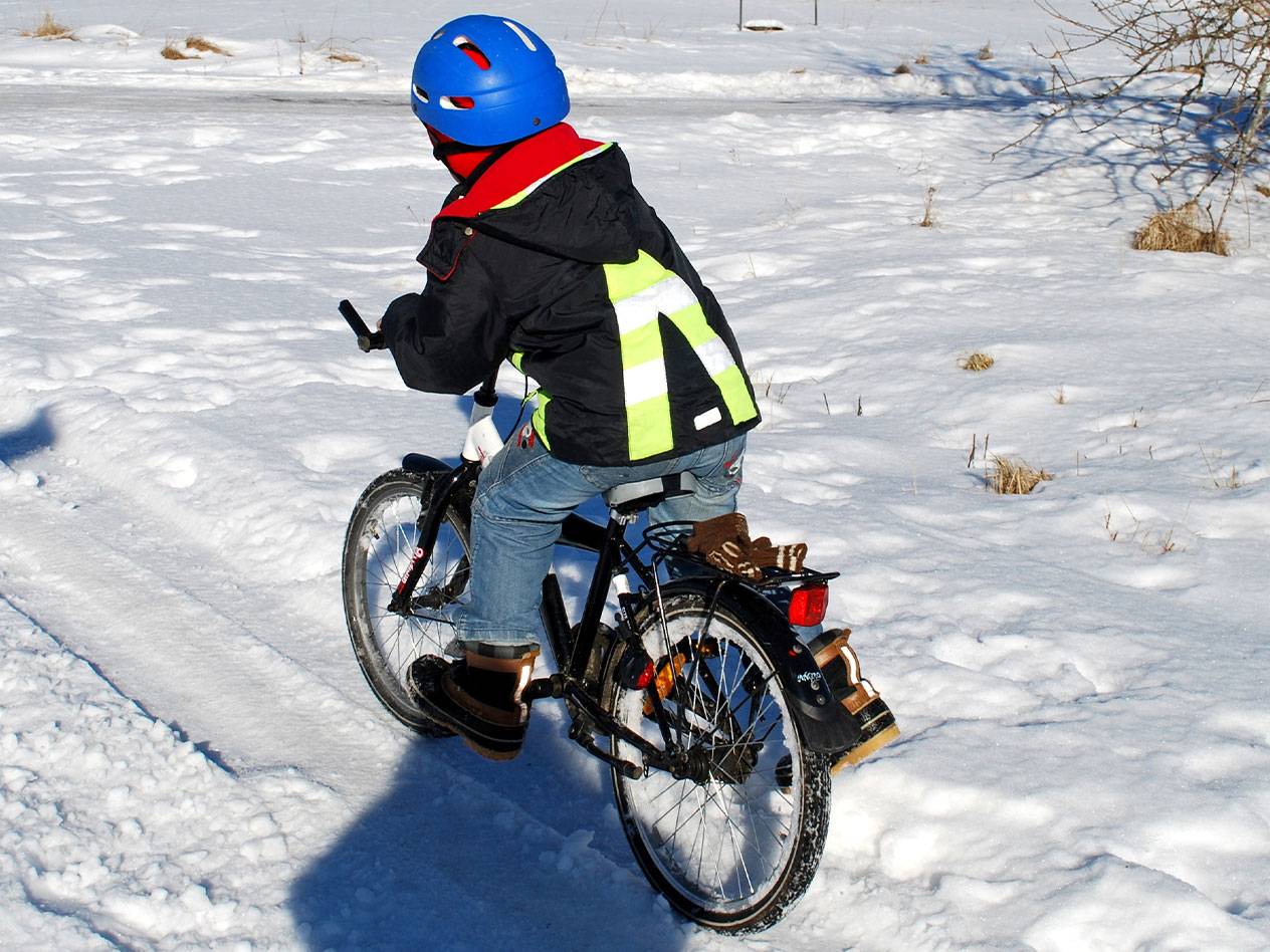 Child with blue helmet and reflective vest riding a bicycle in the snow.