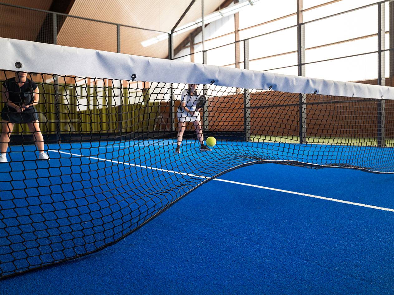 Two women playing padel on a blue court, with the net in the foreground.
