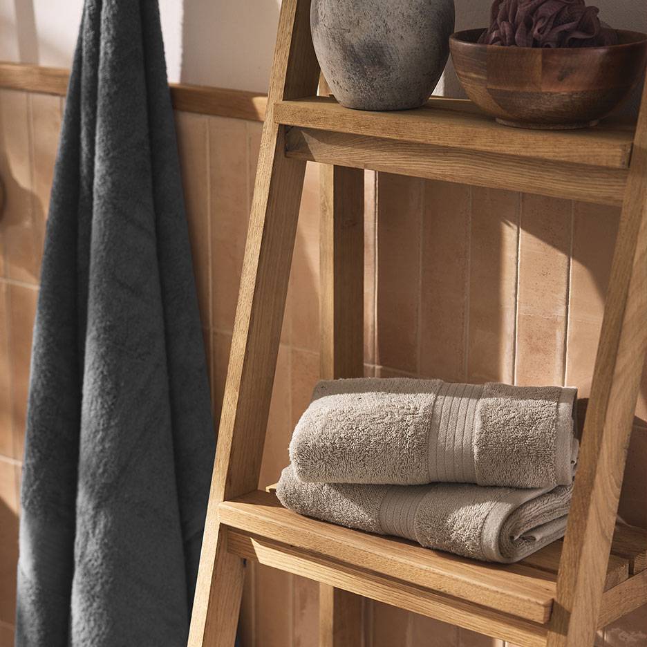 Grey towels on a wooden shelf and ladder in a tiled bathroom.