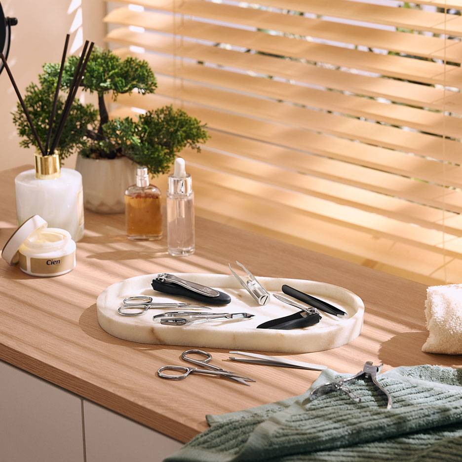Manicure set on marble tray, with cosmetics and plants on a wooden surface.