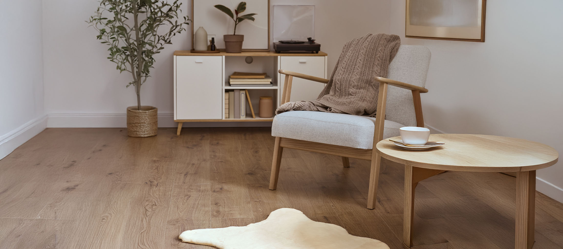 Γκρι υφασμάτινη πολυθρόνα με πλεκτή κουβέρτα, ξύλινο τραπεζάκι σαλονιού και μοντέρνος μπουφές.