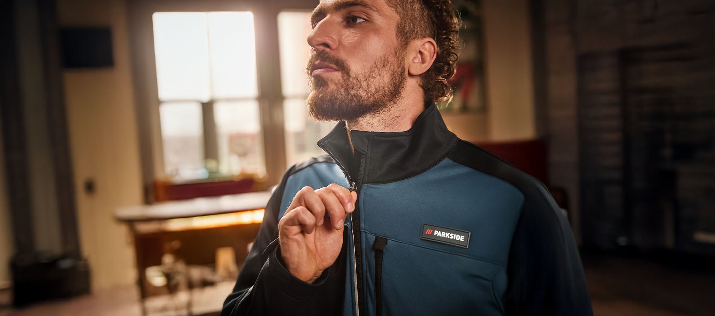 Άνδρας με μπλε και μαύρο μπουφάν εργασίας Parkside το κουμπώνει