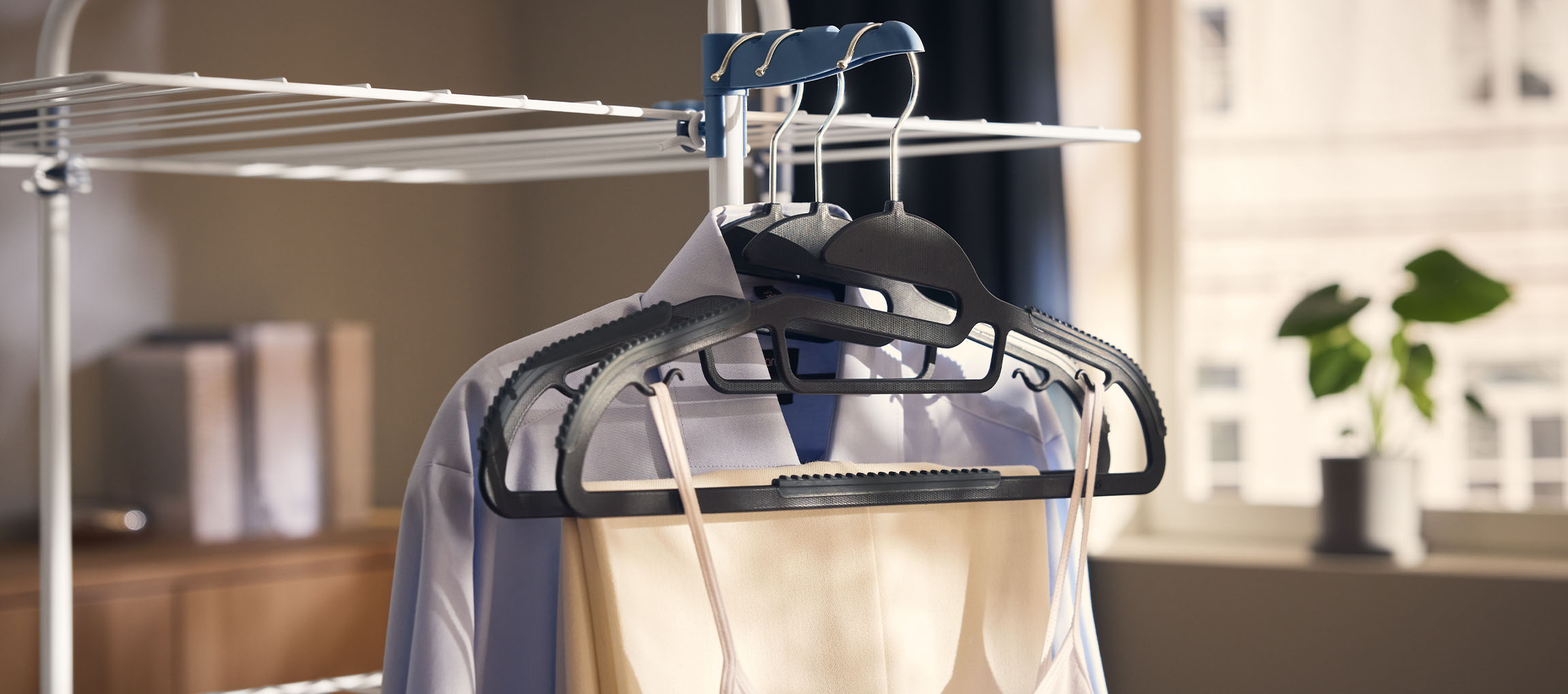 Ρούχα σε κρεμάστρες σε απλώστρα, με φυτό στο παρασκήνιο.