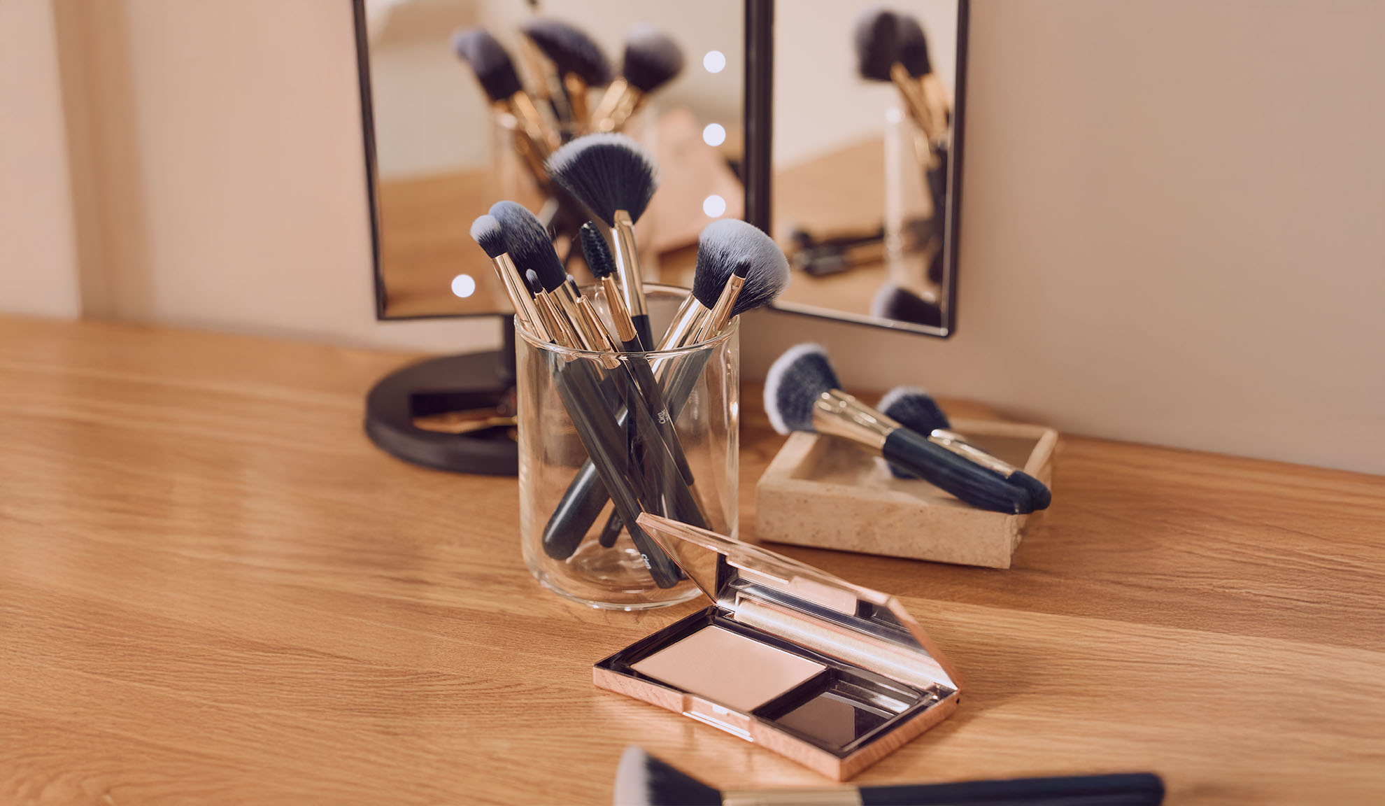 Makeup brushes in a glass jar and powder on a wooden table.