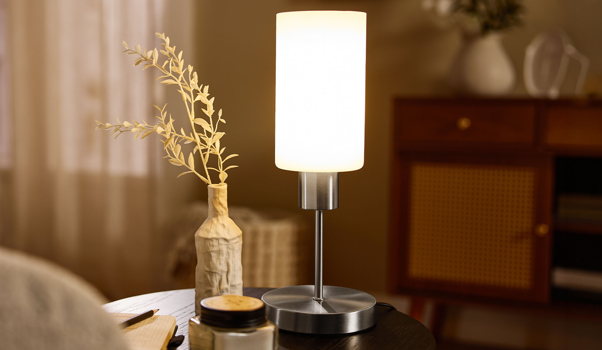 Table lamp with frosted glass and metal, next to a vase with dried plants.