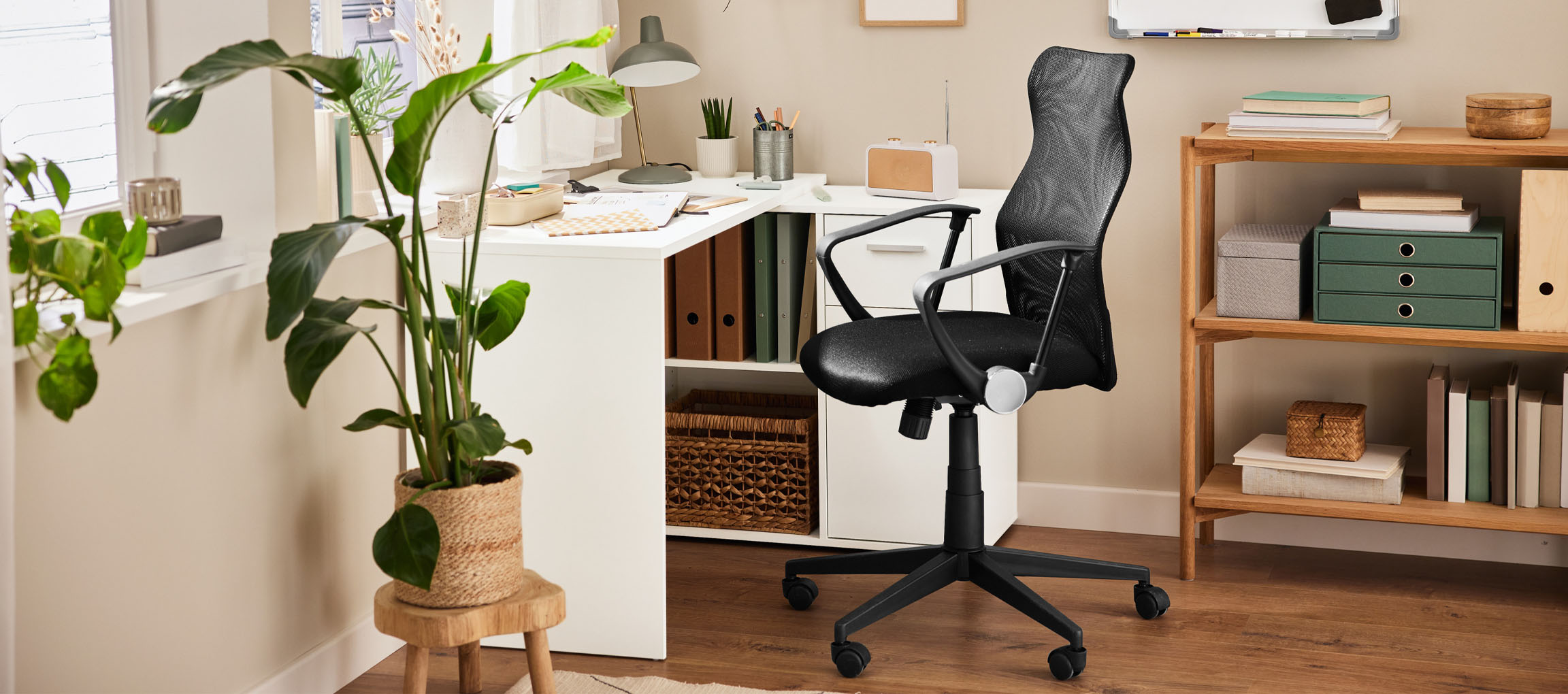 A home office with a white desk, a black office chair, and a wooden bookshelf.