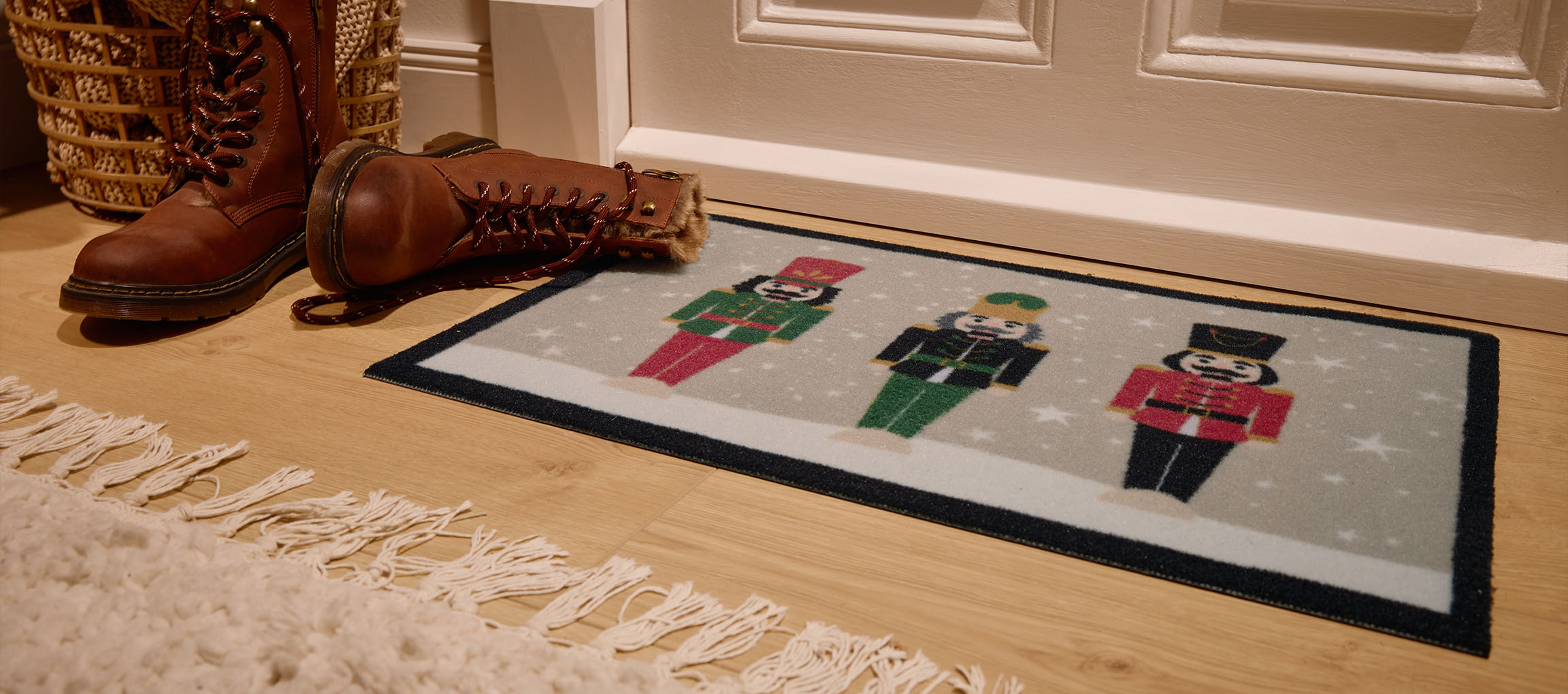 Χριστουγεννιάτικο χαλάκι με καρυοθραύστες, καφέ μπότες και ψάθινο καλάθι στην είσοδο.