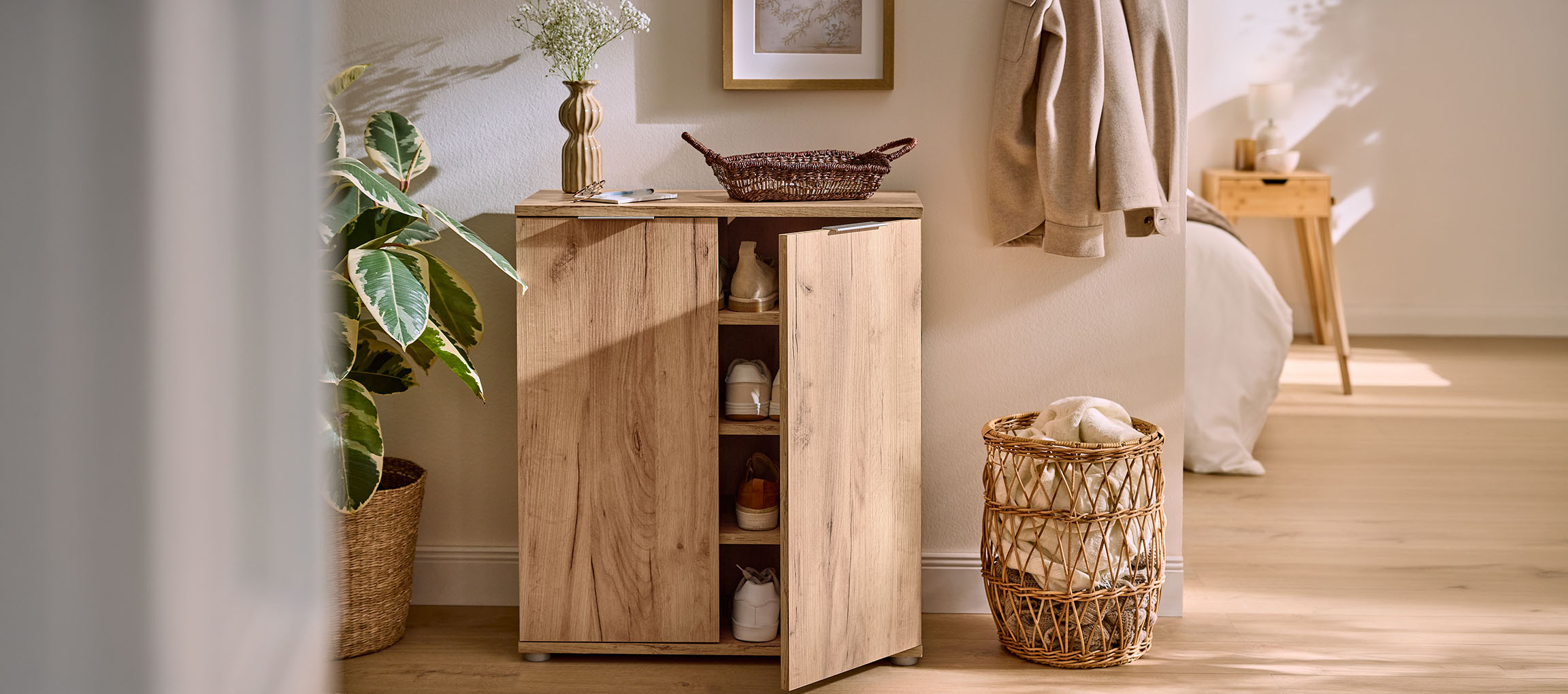 Wooden shoe cabinet with an open door, next to a plant and a laundry basket.