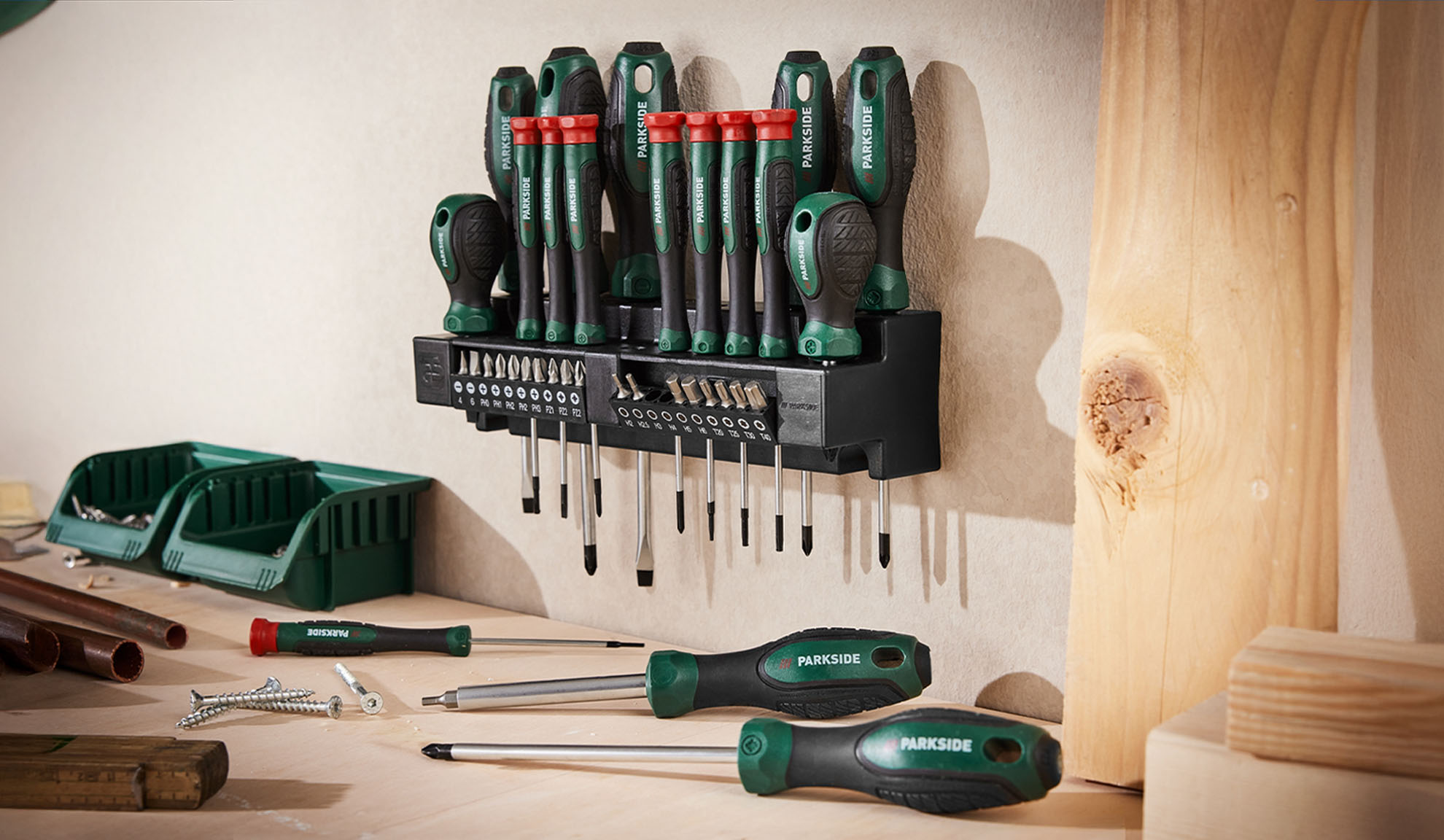 PARKSIDE screwdriver set with various bits, organized on a wall-mounted holder, with additional screwdrivers and tools on a workbench.
