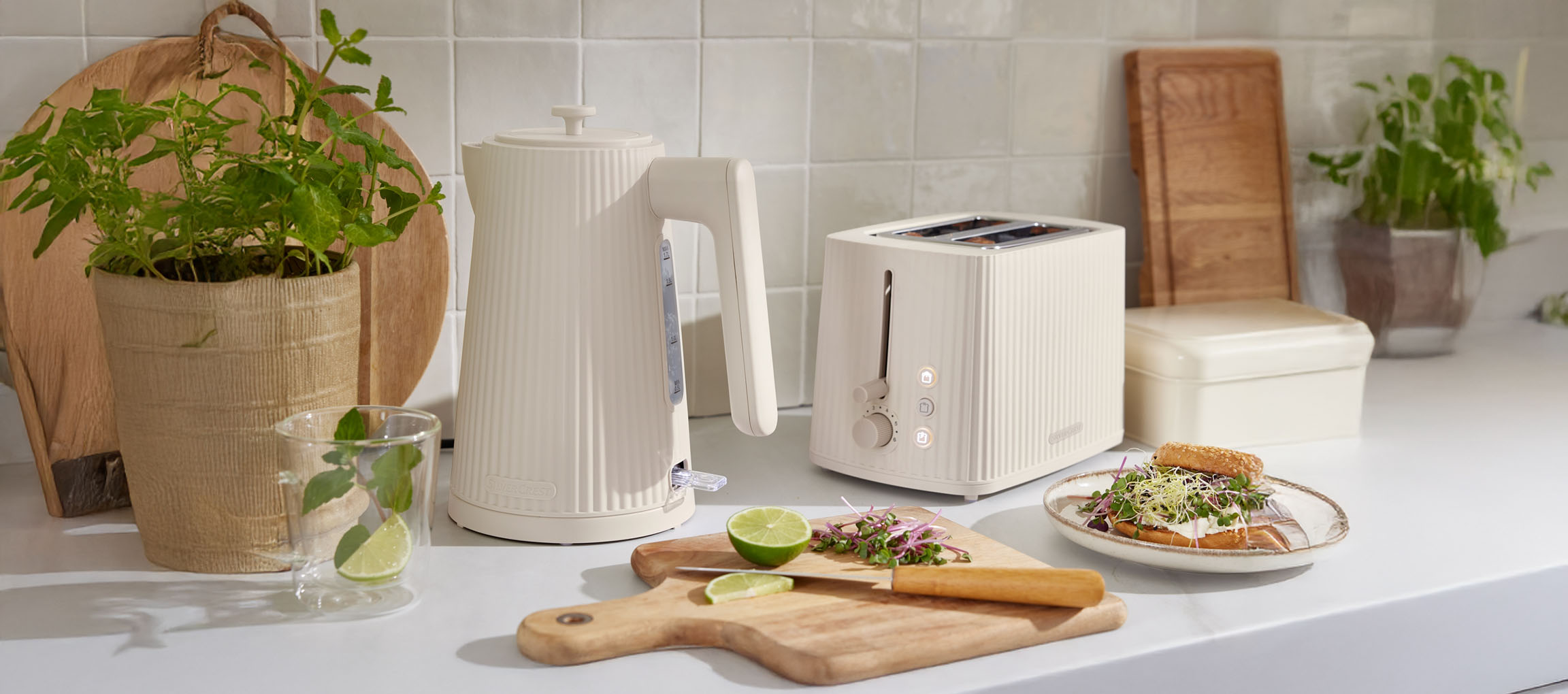 SilverCrest cream-colored kettle and toaster on a kitchen counter with plants and food.