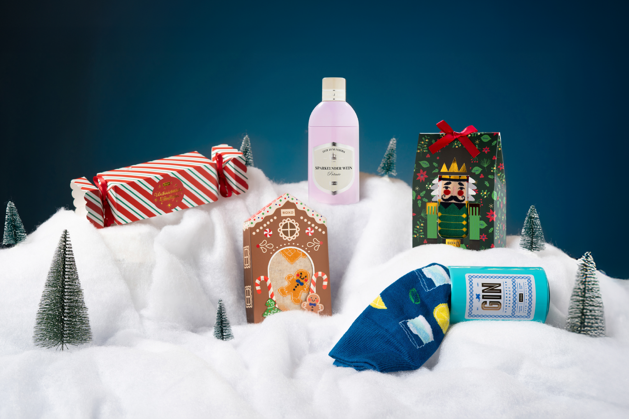 Christmas gifts including Sparkelnder Wein, Gin, and festive socks in a snowy setting.