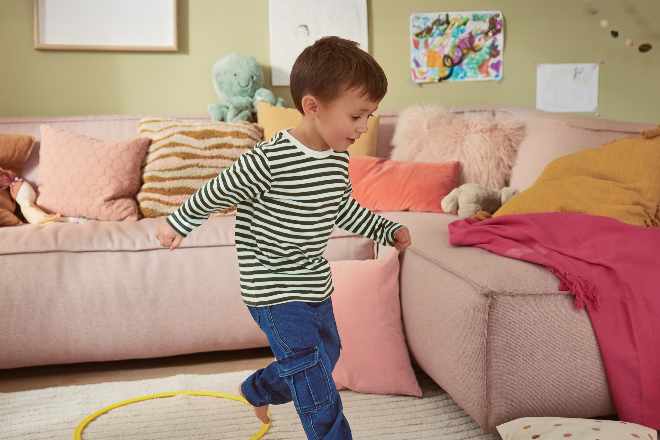 A boy in a striped shirt and jeans playing in a living room with a pink sofa.